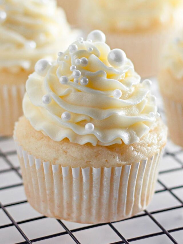 White Wedding Cupcakes on a cooling rack topped with pearl sprinkles.