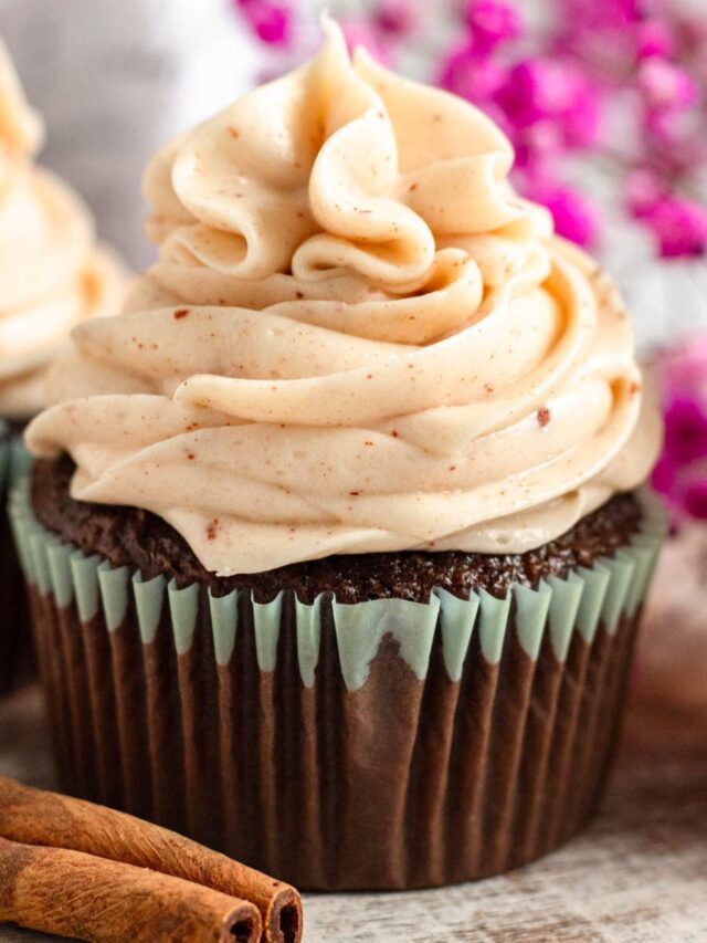 Cinnamon Cream Cheese Frosting piped on top of a chocolate cupcake and surrounded by cinnamon sticks.