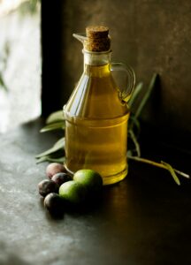 Bottle of olive oil with olives on a table.